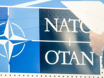 Eine Person mit Klemmbrett steht vor dem NATO-Logo